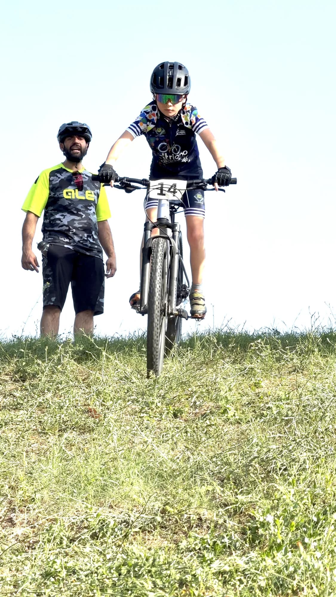 Un maestro della Scuola Triono accompagna a piedi un allievo in mountain bike lungo il percorso di gara