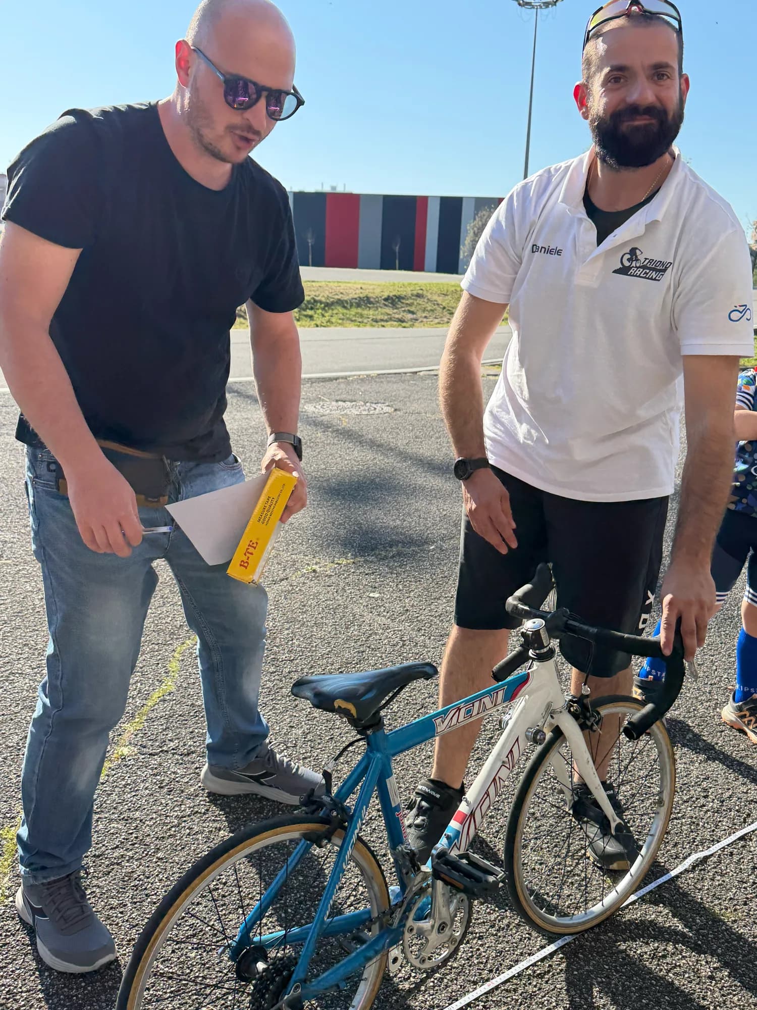 Un maestro della scuola controlla la bici di un allievo insieme a un genitore, prima della lezione di prova.